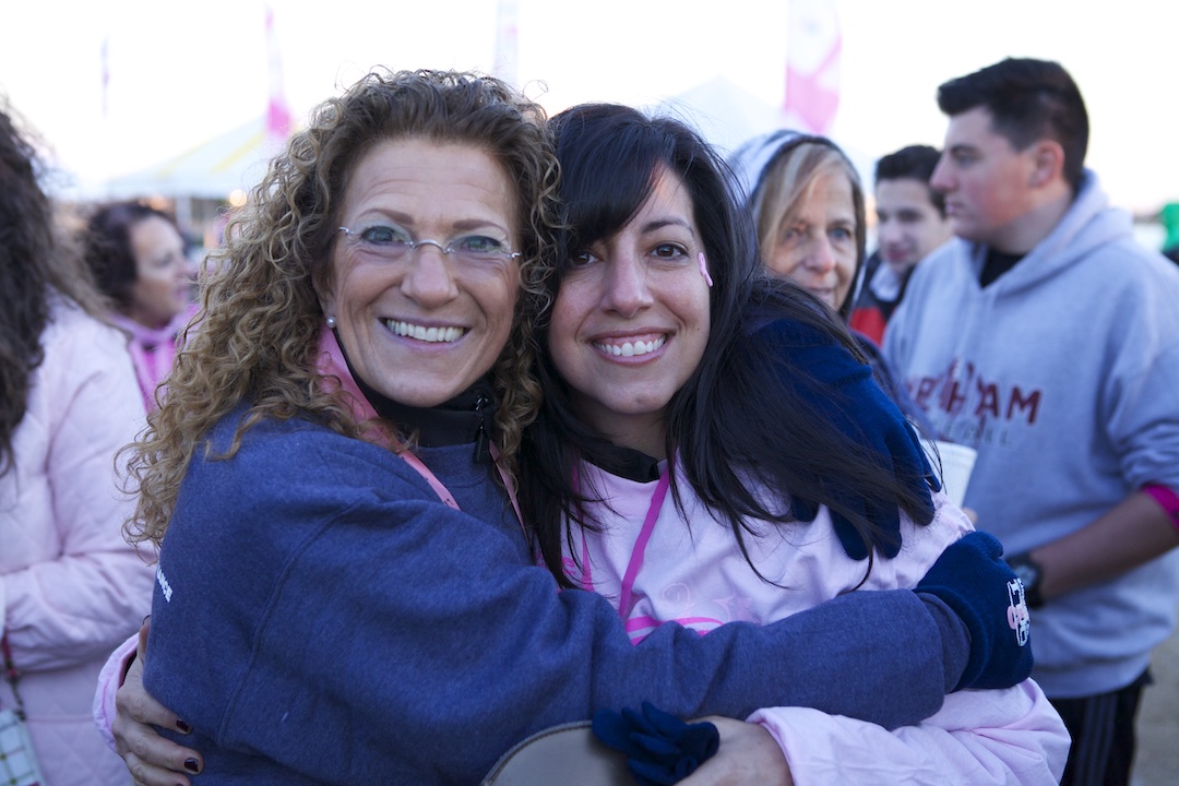 Mollie Sugarman embraces a woman in a pink sweatshirt. People mingle in a crowd in the background