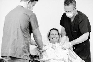 Black and white photo of model smiling happily with eyes closed as Drs. Israeli and Bank on either side prepare the life cast.