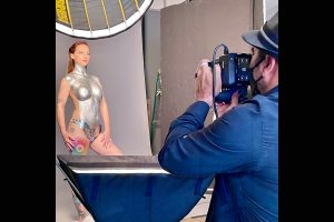 Model posing with silver body paint with photographer in foreground snapping a shot.