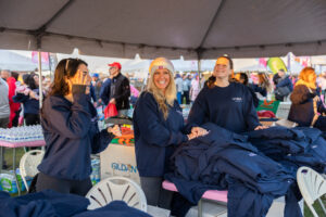 Three women stand under a tent outside with a pile of sweatshirts.