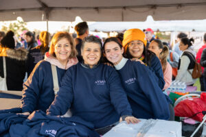 Four women pose together under a crowded outdoor tent.